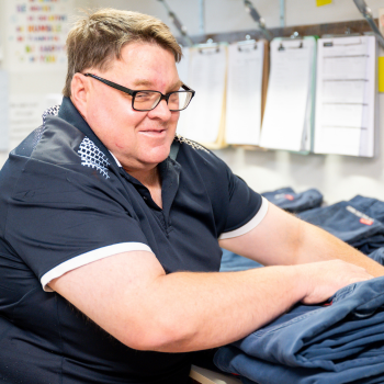 Worker smiling while folding navy garments at a laundry workstation.